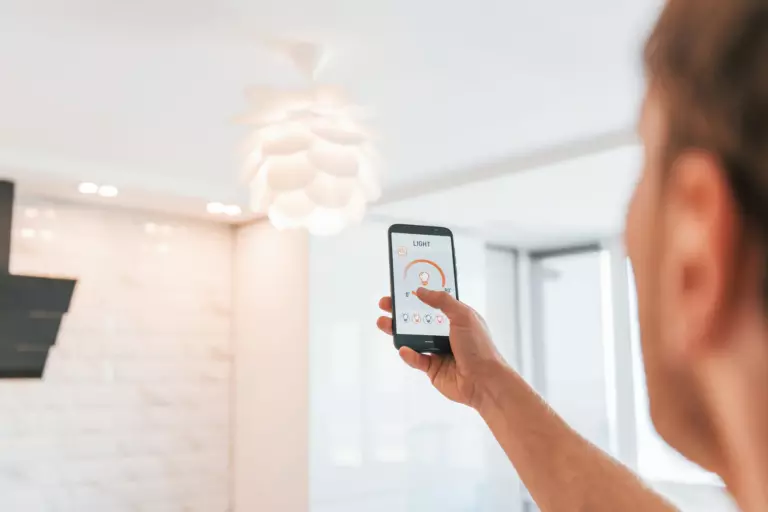 Person holding a smartphone and using an app to control a modern ceiling light in a bright, contemporary room.