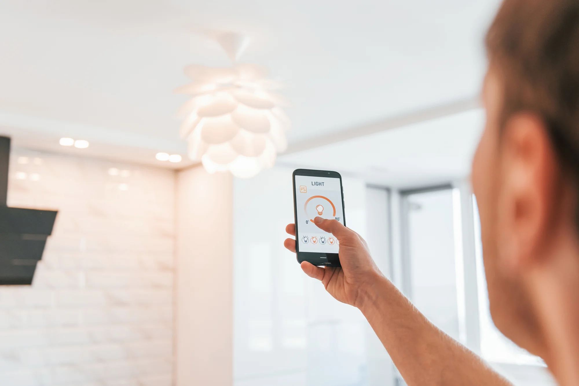 Person holding a smartphone and using an app to control a modern ceiling light in a bright, contemporary room.