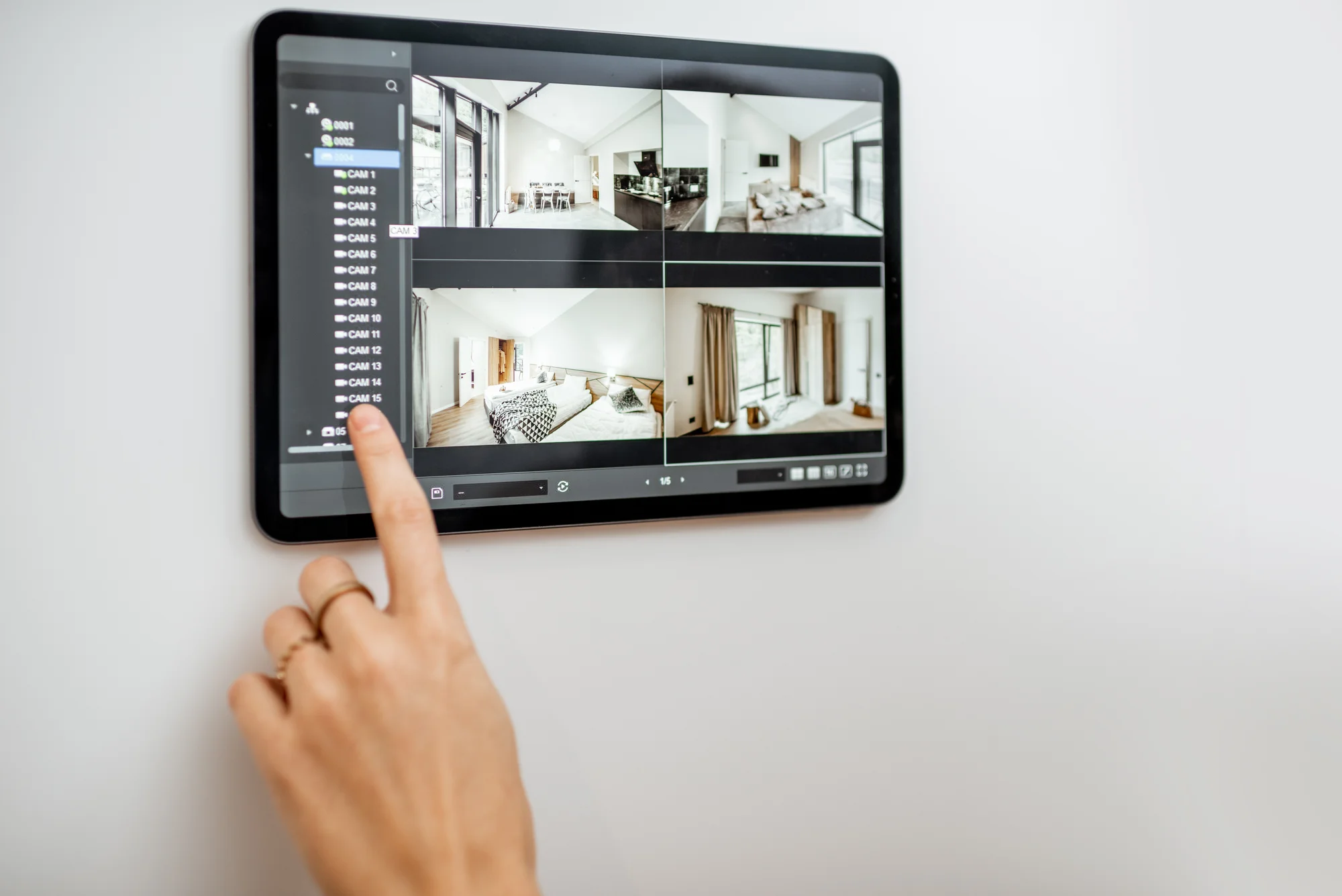 A person operates a wall-mounted touchscreen displaying live security camera feeds of different rooms in a house.