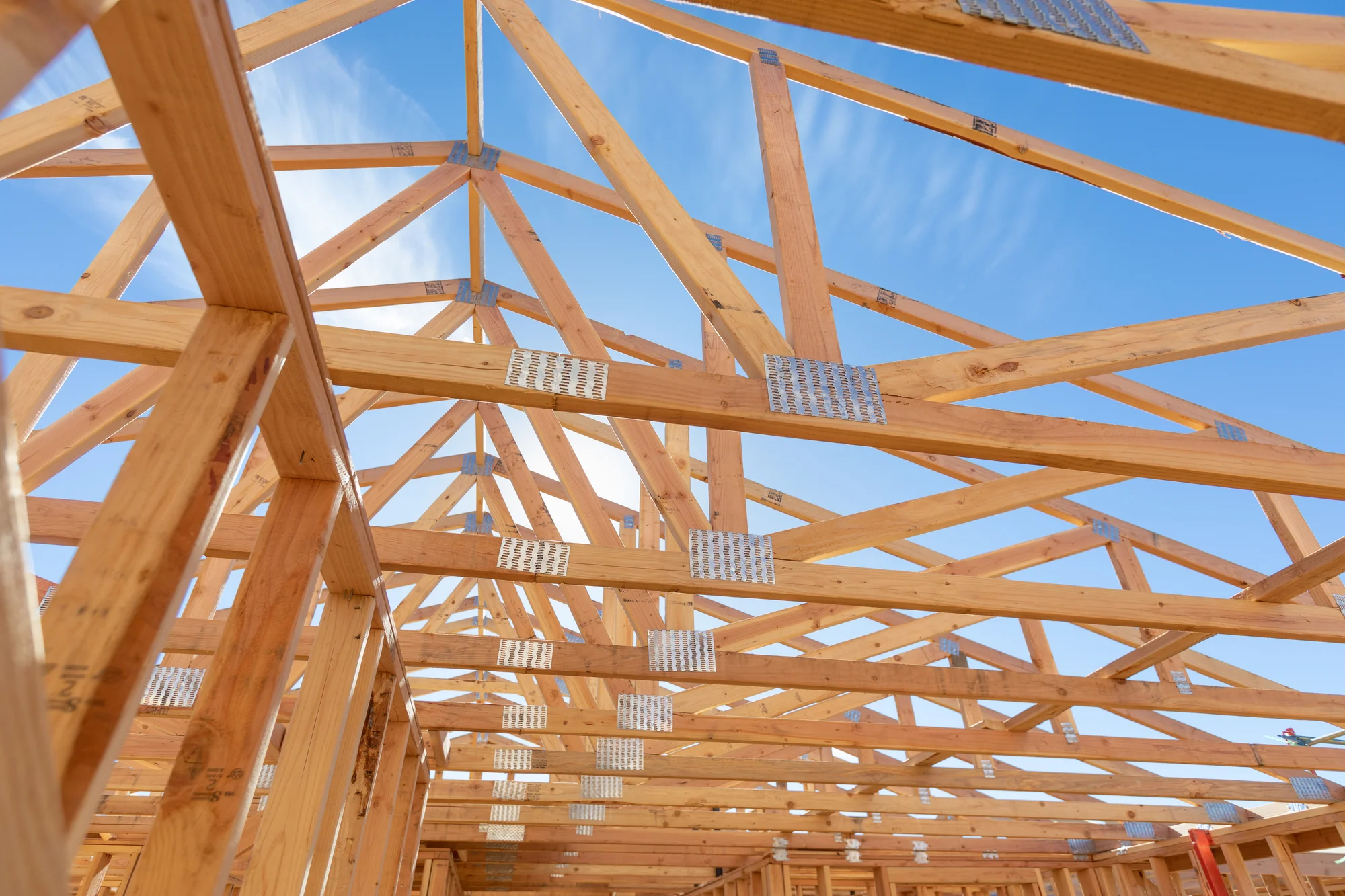 Exposed wooden roof trusses under construction, with metal connectors, against a clear blue sky.